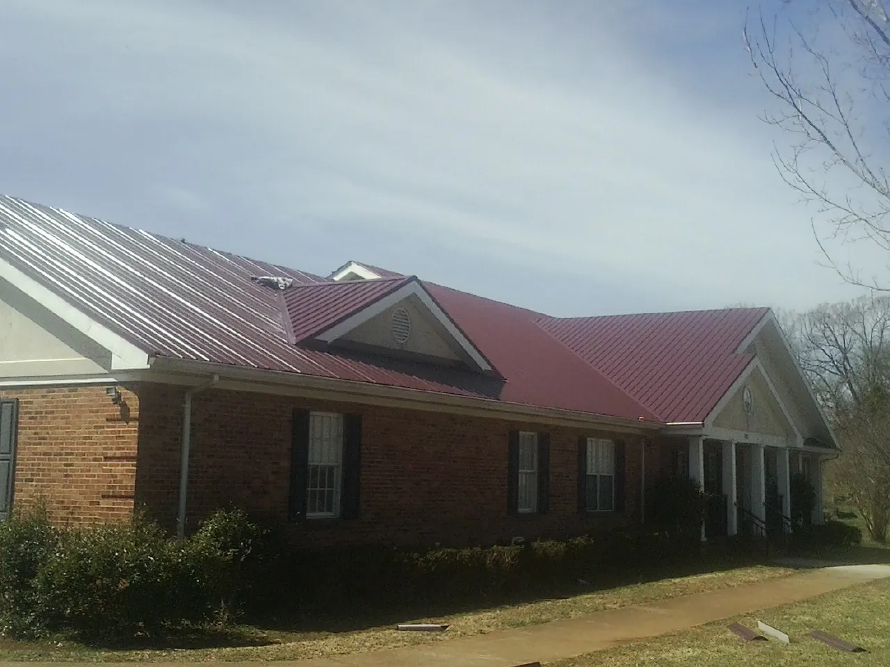 Red metal roof with gabled entries on a long brick building, from a Hail Damage Roof Repair job in Louisville